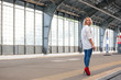 © Sergey - young beautiful girl in a white shirt, blue jeans and red shoes goes on the platform at the old railway station