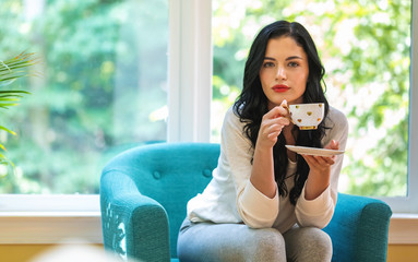 Wall Mural - Young woman drinking coffee in a chair in her home