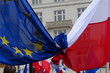 Flaga Unii Europejskiej i Polski splecione, związane razem, podczas demonstracji poparcia dla członkostwa Polski we Wspólnocie, w tle, rozmyte, budynki, inne flagi, głowa mężczyzny, z tyłu