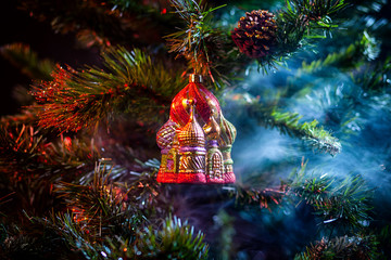 Red shiny decoration Christmas balls Kremlin with house in colored purple-red smoke, on an  christmas tree background. Concept of a modern Christmas card.