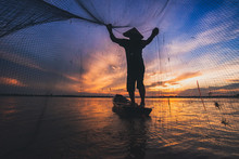 Asian Fisherman On Wooden Boat Casting A Net For Catching Freshwater Fish In Nature