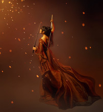 Young Kunoichi Girl Samurai In A Long Dress With A Lotus Tattoo On The Back, Holding Katana In Hands. The Child Of War, Princess Becomes A Warrior. Art Photo In Orange And Brown Colors, Glare, Sparks.