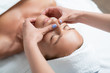 © Yakobchuk Olena - Feeling sleepy. Close up portrait of charming woman with closed eyes enjoying skincare procedure at spa salon. Masseuse hands with blue manicure touching client chin and nose