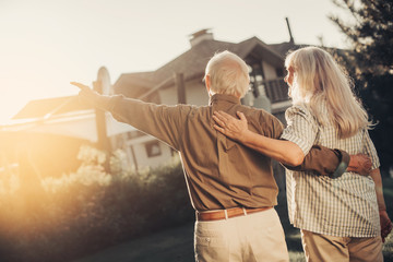 Bright future. Cheerful twosome embracing and looking up man pointing at. They standing back to camera on lawn fronting house. copy space on left side