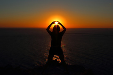 Wall Mural - young girl is facing the sun on the mountain and looking at the sea, hands raised up and to the side