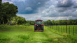Farming: Large red tractor mowing green farmers pasture along barbwire fence