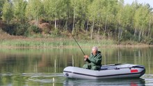Senior Fisherman Floats On A Lake On An Inflatable Boat With A Fishing Rod
