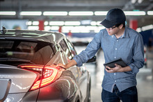 Asian Auto Mechanic Holding Digital Tablet Checking Tail Light In Auto Service Garage. Mechanical Maintenance Engineer Working In Automotive Industry. Automobile Servicing And Repair Concept