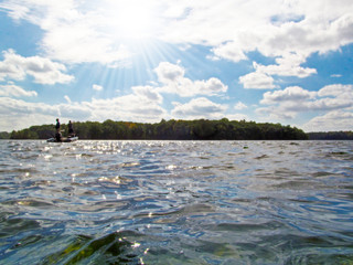 Beautiful lake or river in the park on a sunny day. A trees, a water surface, a view on a boat with two fishermen in the distance.