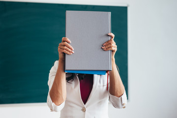 Wall Mural - Female student standing near blackboard with book