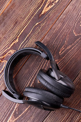 Wall Mural - Headphones on wooden background, vertical image. Black earphones on textured wooden surface with text space, top view. Stereo volume equipment object.