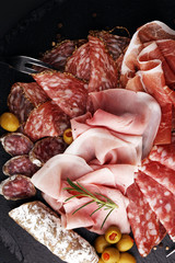 Marble cutting board with prosciutto, bacon, salami and sausages on wooden background. Meat platter