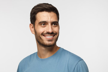 Wall Mural - Close up portrait of smiling handsome male in blue t-shirt looking right, isolated on gray background
