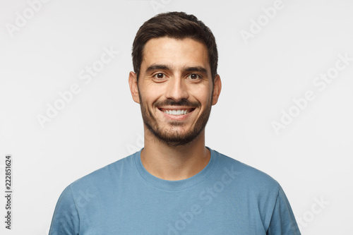 Cuadros en Lienzo Close up portrait of young smiling handsome guy in blue t-shirt isolated on gray