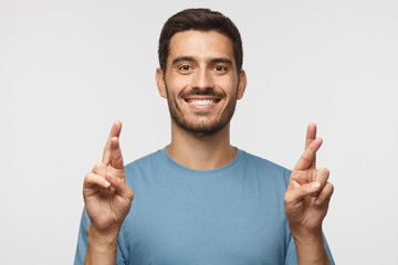 Wall Mural - Closeup portrait of handsome caucasian male isolated on gray background, looking at camera, crossing fingers for luck