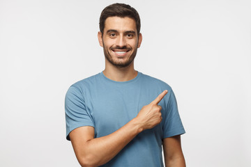 Wall Mural - Young man in blue t-shirt pointing right with his finger isolated on gray background