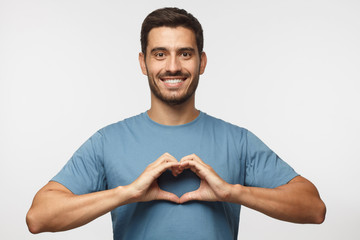 Wall Mural - portrait of young smiling man in blue t-shirt showing heart sign isolated on gray background