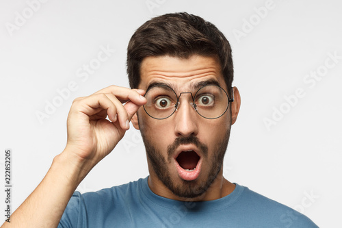 Fotografía Young man in blue t-shirt shouting oh my god with open mouth, holding round glas
