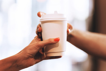 Barista passes coffee to a visitor in a popular coffee shop, hands and a glass of coffee are shot close-up.