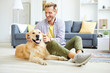 © pressmaster - Cheerful young man in casualwear relaxing at home and playing with friendly purebred golden labrador