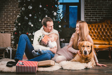 Wall Mural - theme Christmas and New Year family circle and domestic pet. Mom dad and child 1 year old Caucasian woman sitting on floor near Christmas tree with gifts and big dog breed labrador golden retriever