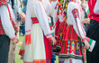 Unrecognizable irls in ethnic Bulgarian costumes with colorful ornament holding a flag of Bulgaria. Sunset at the background