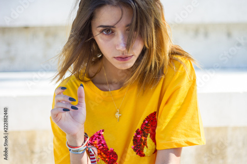 Fotomural Young woman posing on the street wearing a yellow shirt while the sun is shining