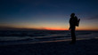 © Joshua - Guy stands in front of dramatic sunset over the ocean on a beach covered with waves.
