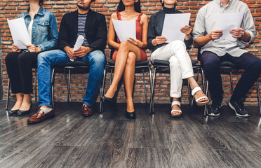 Group of business people holding paper while sitting on chair waiting for job interview against brick background