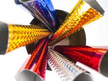 Closeup Photograph Looking Down At Several Multi-colored Holographic Paper And Plastic New Year's Eve Celebration Horns Inside Of A Round Can Including Red, Yellow, Blue, And Silver.
