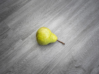 A single ripe yellow pear and stem on a gray wood grain background.