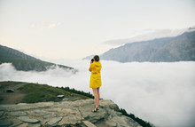 A Young Girl In A Yellow Raincoat Photographs The Mountains. Georgia. Summer. August. Girl Making A Photo Shoot Of Mountain. 
