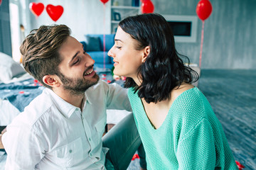 Beautiful young tender lovely couple are kissing and hugging each other while sitting on the floor of bedroom with romantic background. St Valentine's day. Anniversary. Date. Love concept