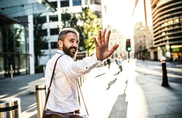 Canvas Print - Hipster businessman walking up the street in London, looking back and greeting somebody.