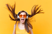 Portrait Of Excited Cheerful Laughter Funny Comic Woman In Orange Glasses In Headphones With Fluttering Hair Isolated On Yellow Background. People Sincere Emotions, Lifestyle Concept. Advertising Area