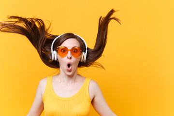 Portrait of excited cheerful laughter funny comic woman in orange glasses in headphones with fluttering hair isolated on yellow background. People sincere emotions, lifestyle concept. Advertising area