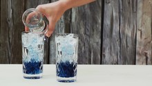 Pouring Soda Water Into Two Crystal Glasses Filled With A Concentrated Blue Pea Flower Tea Syrup And Ice Cubes