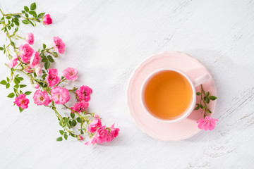 Cup of tea and branch of small pink  roses on rustic table. Flat lay