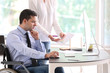 © Pixel-Shot - Businessman in wheelchair working with colleague in office