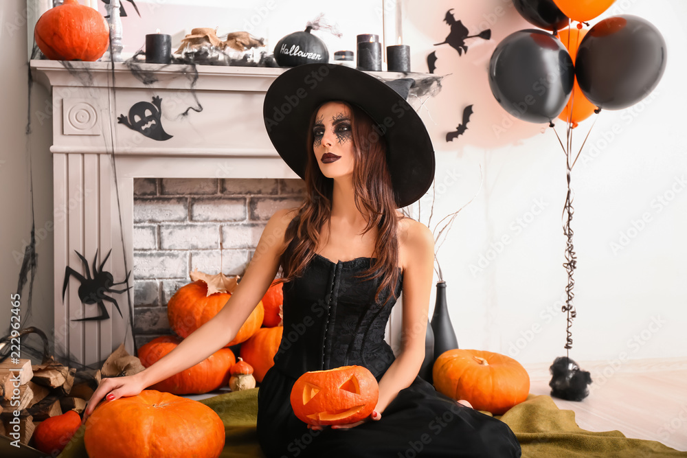 Beautiful woman dressed as witch in room decorated for Halloween