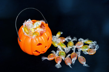 halloween Jack o Lantern candy collector full of candy and some scattered sweets on the black background