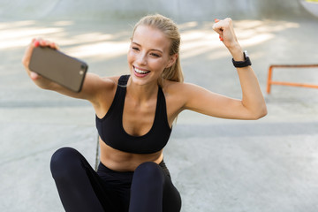 Wall Mural - Sports woman sitting outdoors take a selfie by mobile phone.