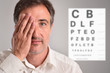 Middle-aged man covering an eye for optical revision letter chart