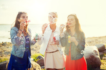 summer vacation, holidays, fun and people concept - group of happy young women or teenage girls blowing bubbles on beach