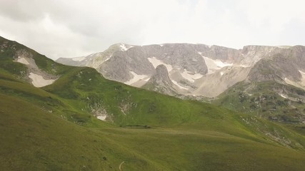 Wall Mural - snowy mountain peaks and green meadow landscape aerial view from flying drone