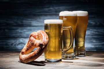 Wall Mural - three glasses of beer with foam and tasty pretzel on tabletop, oktoberfest concept