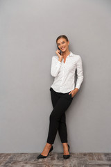 Wall Mural - Happy business woman standing over grey wall background talking by mobile phone.