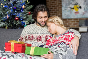 beautiful young couple holding christmas gifts and sitting together on couch