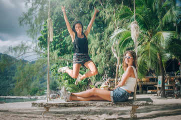 Wall Mural - Two beautiful girlfriend enjoy a swing and drink coconut