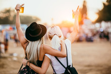 Two Female Friends Drinking Beer And Having Fun At Music Festival.Back View